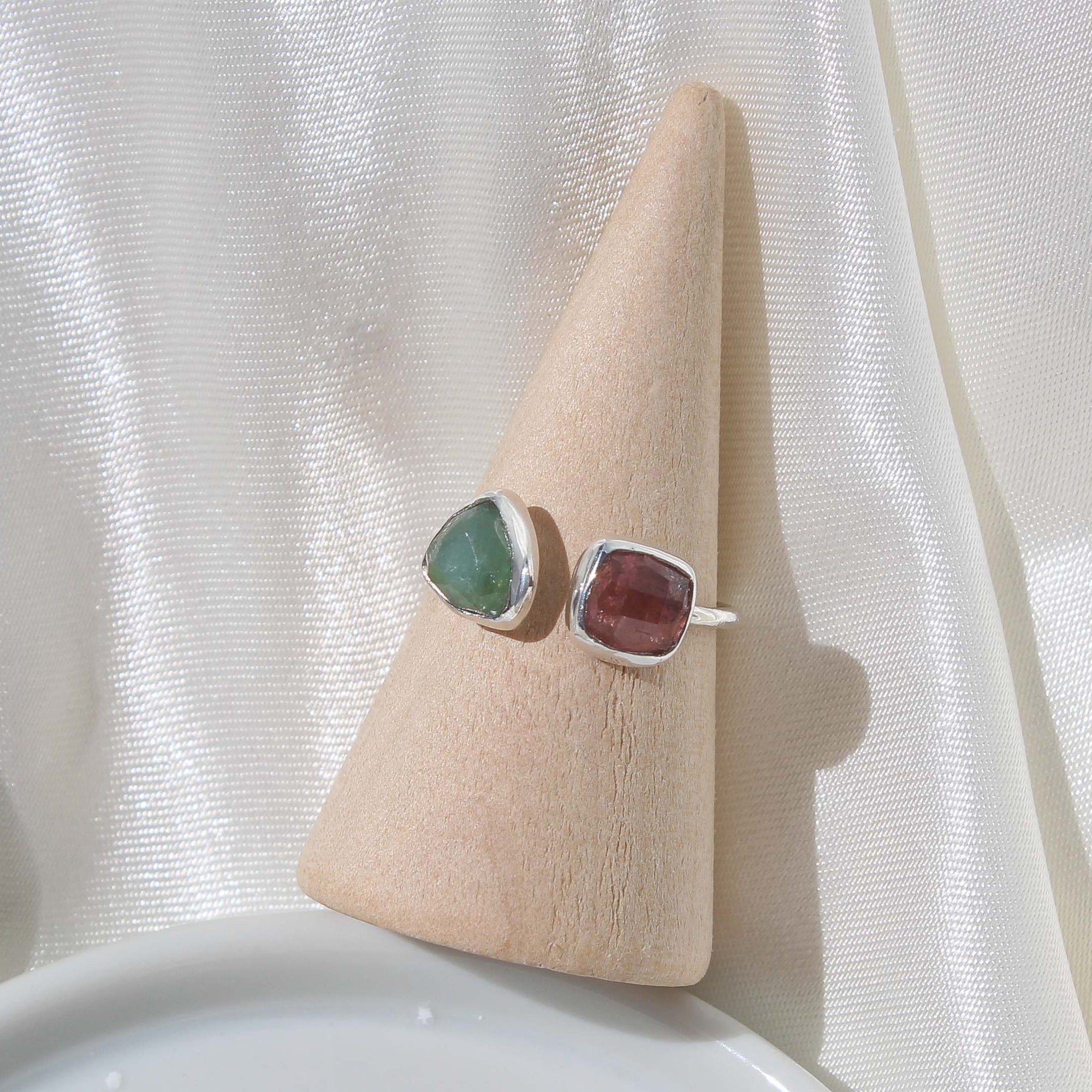 925 sterling silver adjustable ring with a simple band, a faceted triangular shaped green tourmaline on the left side and a faceted square shaped pink tourmaline stone on the right side.